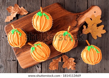 Autumn pumpkin cupcakes on a wooden serving platter. Above view on a rustic wood background.