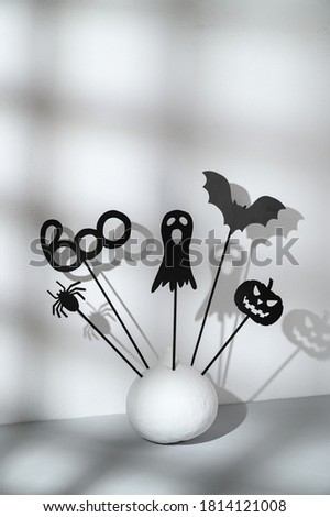 Halloween home decorations. Painted white pumpkin and black Halloween frightening puppets on sticks on a light gray background. Abstract shadow. Copy space, vertical orientation. Isometric style.