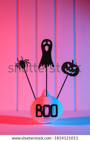 Halloween home decorations. Painted white pumpkin and black scary Halloween puppets on sticks, illuminated with neon light. Copy space, vertical orientation.