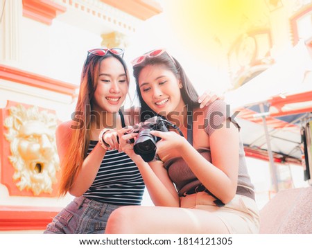 Two pretty Asian women are checking photos on the camera together in an amusement park.
