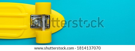 Minimalist flat lay photo of yellow plastic mini cruiser board on blue background. Top view of bright yellow cruiser skateboard with copy space.