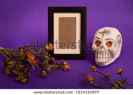 Day of the dead, mexican tradition concept with photo frame for remembrance, sugar skull and dry flowers on violet background
