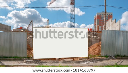 blank white information board on iron fence of construction site with crane outside