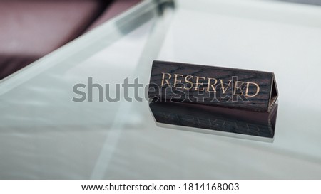 Close up shot of wooden reserved sign on the glass dining table in restaurant. Reservation seat for dating or dinner. Image with copy space.