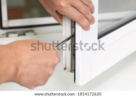 handyman adjusting white pvc plastic window indoors. worker using screwdriver to repair upvc window. homework maintenance. Royalty-Free Stock Photo #1814172620