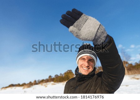 People, christmas, winter and season concept - happy smiling man in jacket and winter hat enjoying sunny winter day.