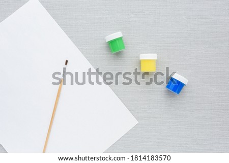 Brush, multi-colored set cans of paint, empty sheet of paper on grey background. no people. Top view. copy space. Workplace artist. drawing kit. fine art, creativity, painting, artistic tools concept