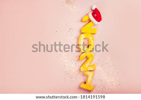 Happy New Year 2021. Golden digits 2021 with christmas hat are on pink background with glitter. Holiday Party Decoration or postcard concept with top view and copy space.
