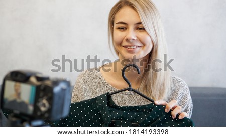 Fashion blogger recording video for blog. Woman in front of the camera holding a green dress in her hands. Close up portrait
