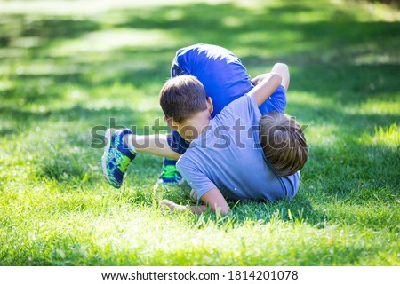 Two boys fighting outdoors. Siblings or friends wrestling on grass in summer park. Siblings rivalry.