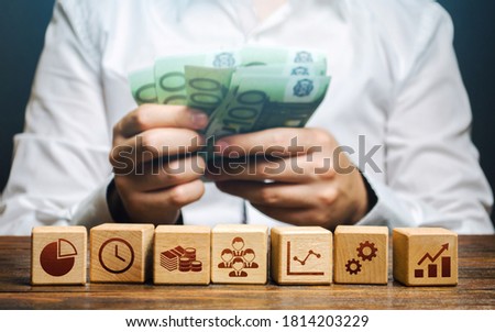 A man is counting money and blocks with business attributes. Good business model. Profitability. The rules for successful investment. High performance, great work. Company management Royalty-Free Stock Photo #1814203229