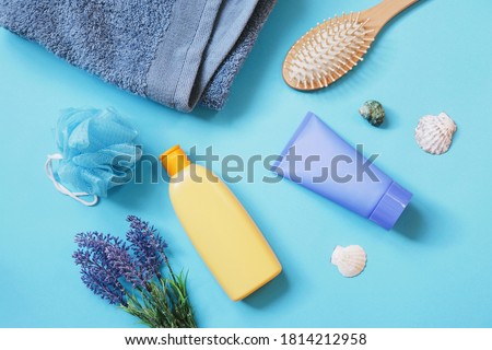 Blue towel, sponge, orange shampoo bottle, moisturizing facial cream, wooden comb and lavender flowers. Flat lay beauty photography natural organic cosmetics