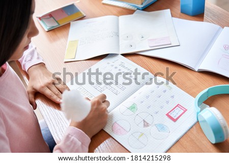 Over shoulder view of indian latin preteen primary school girl student, child pupil studying at home sitting at desk writing math, doing homework, learning at table with exercise books and supplies. Royalty-Free Stock Photo #1814215298