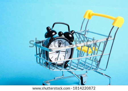 alarm clock in miniature shopping trolley on blue background copy space