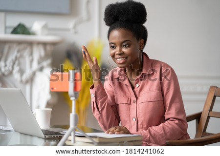African American millennial woman with afro hairstyle remote studying, working online on laptop, chatting with friends via video call on smartphone on tripod. Blogger influencer recording video blog. Royalty-Free Stock Photo #1814241062