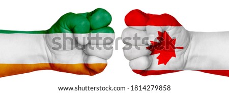The concept of the struggle of peoples. Two hands are clenched into fists and are located opposite each other. Hands painted in the colors of the flags of the countries. Canada vs Cote DIvoire