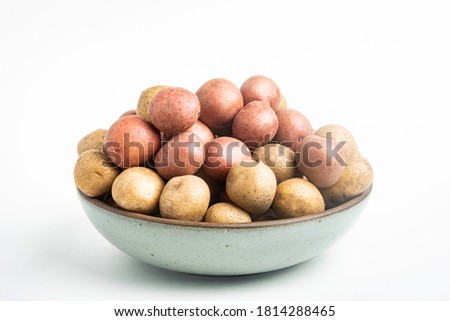 Raw and fresh baby potatoes artfully arranged in a bowl and set on white background.