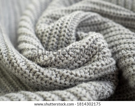 Knitted warm grey sweater or scarf. Cozy composition in the home atrosphere. Wool fabric texture close up background. Comfortable style cloth. Wavy folds material. Soft focus Royalty-Free Stock Photo #1814302175