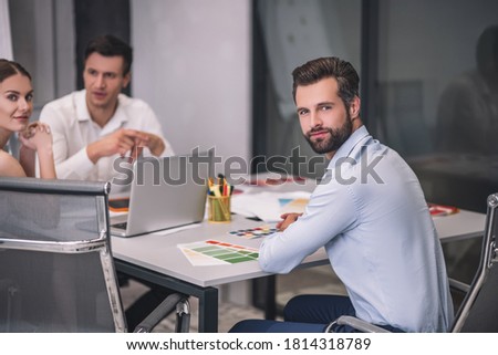 Fashion studio. Bearded male sitting at table opposite his male and female coworkers