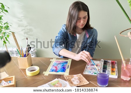 Teenager girl painting with watercolors, sitting at home at the table. Art, education, creativity, teenage hobbies