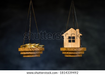 The scales with the coins and the home of the imitation of bamboo. The concept of purchasing housing, credit, and quotes on the real estate market. Royalty-Free Stock Photo #1814339492