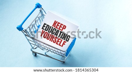 Shopping cart and text KEEP EDUCATING YOURSELF on white paper note list. Shopping list concept on blue background.