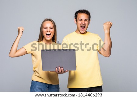 Portrait of a satisfied happy couple holding laptop computer while standing and celebrating isolated over gray wall background