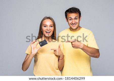 Happy surprised couple showing blank credit card and pointing at you, over grey background