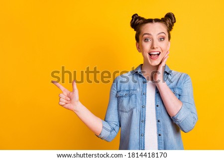 Photo of charming funny excited teen lady two buns direct finger side empty space show novelty shopping banner low prices season wear casual denim shirt isolated yellow color background
