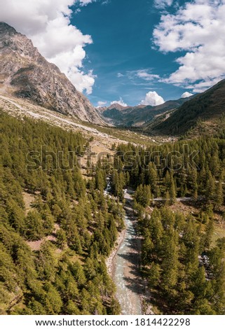 Aerial drone photo of a beautiful alpine valley. The drone flies over pine forests and the glacier melt water river that snakes along the valley floor.