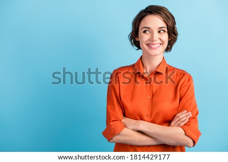 Photo of funny attractive cheerful lady bobbed hairdo arms crossed self-confident person worker good mood look side empty space sly eyes wear orange office shirt isolated blue color background