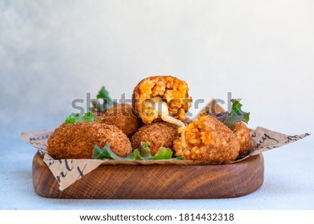 Rice balls stuffed with mozzarella cheese and deep fried on a wooden plate. Light background. Royalty-Free Stock Photo #1814432318