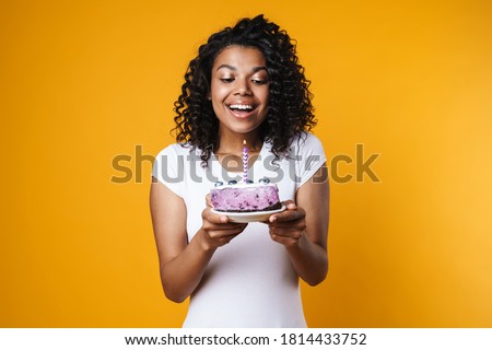 Image of happy african american woman holding birthday cake with candle isolated over yellow background