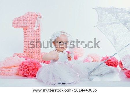 Birthday celebration: child sitting on the floor among the decoration: numbers 1, artificial flowers and gifts. The concept of birthday, holidays. copy space