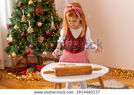 Little girl having fun at home during winter holiday season, standing by nicely decorated Christmas tree and making Christmas cookies