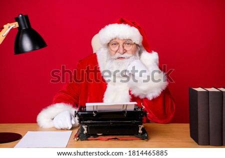 Photo of santa claus grey beard sit desk fist cheek vintage typewriter lamp paper book wear x-mas costume coat cap glasses isolated red color background