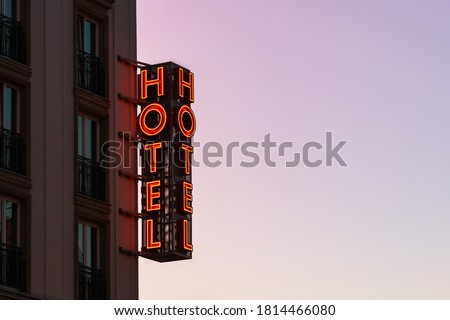 Neon hotel sign on the building corner against the sunset sky Empty copy space for inscription. Vintage sign. Vertical hotel sign