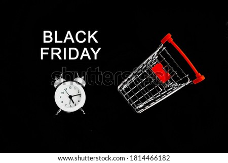 White alarm clock, shopping cart, and black Friday sign on a black background. Theme of sales and discounts.