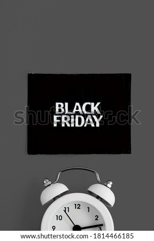 white alarm clock and an inscription on a black square - black Friday on a gray background. The topic of sales.