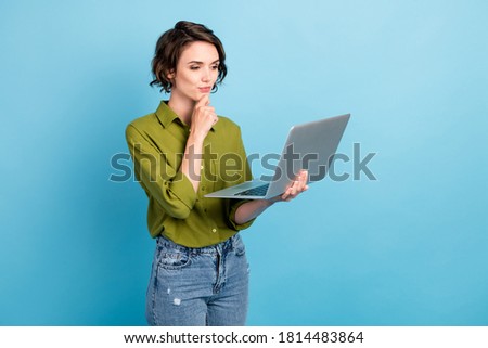 Photo of charming lady short hairdo hold netbook finger chin look screen wear jeans green shirt isolated blue color background