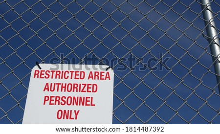 Restricted area, authorized personnel only sign in USA. Red letters, keep off warning on metal fence, United States border symbol. No trespassing notice means violators will be prosecuted by US law.