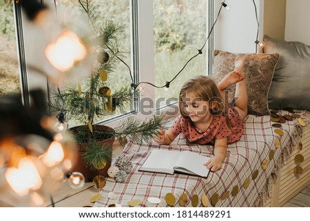 little girl writes in a notebook. The child sits on the windowsill. Christmas and New Year concept. High quality photo