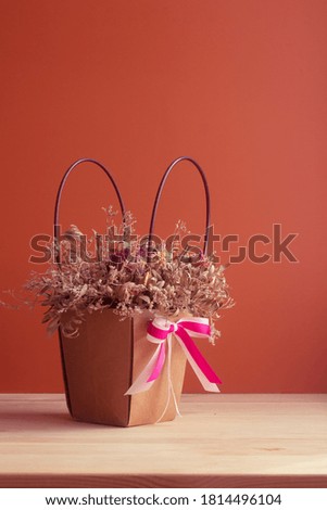 dried bouquet of flowers in a pink tinted paper basket with a bow on a orange background
