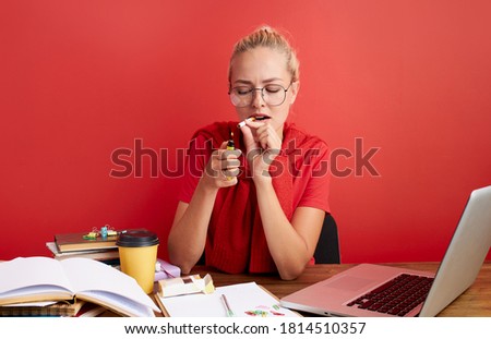 young caucasian blonde female smoke cigarette at work place, have no time to deadline, isolated red background