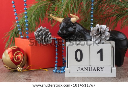 calendar with the date January 01 and a bull figurine. Handmade wood cube with date month and day. Festive Christmas decorations on a red background. bull as a symbol of the new year 2021. 