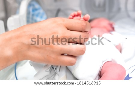 Nurse takes action to monitor and care for premature baby, selective focus - baby foot and nurse arm. Newborn is placed in the incubator. Neonatal intensive care unit Royalty-Free Stock Photo #1814516915