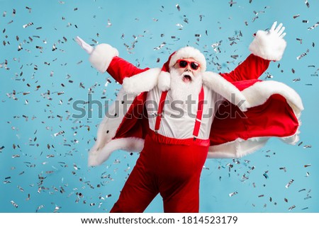 Photo of pensioner old man grey beard carefree raise hands dance open mouth pretend flying angel confetti wear santa x-mas costume suspender sunglass headwear isolated blue color background