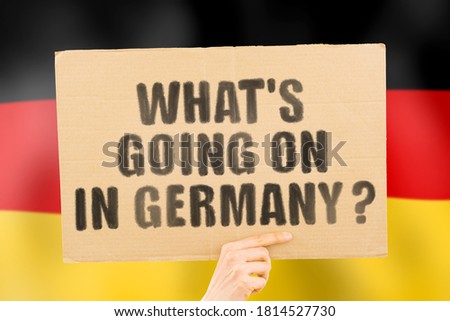 The question " What's going on in Germany? " on a banner in men's hand with blurred Deutsch flag on the background. Protests on the street. Riot. Violence. Economic crisis. Collapse. Politics