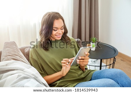 Young african woman sitting on grey couch and working at home with tablet.