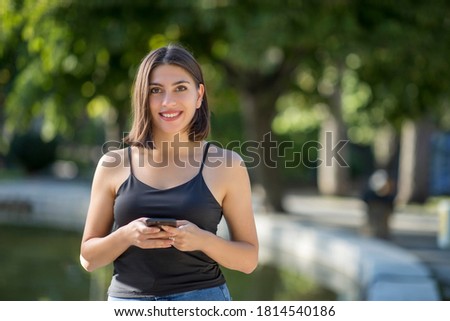 Young beautiful Turkish woman is checking mobile phone while smiling and she is looking to camera